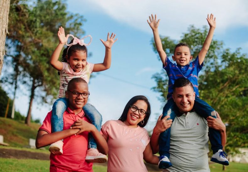 A joyful family spending quality time outdoors with kids on parents' shoulders.
