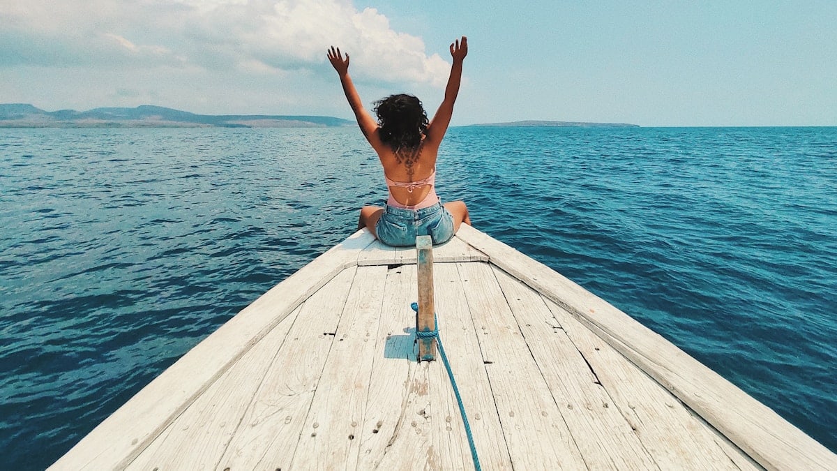 woman wearing blue denim short-shorts sitting on boat raising hands